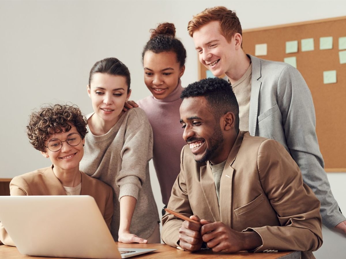 Cinco profissionais reunidos em torno de um notebook, sorrindo