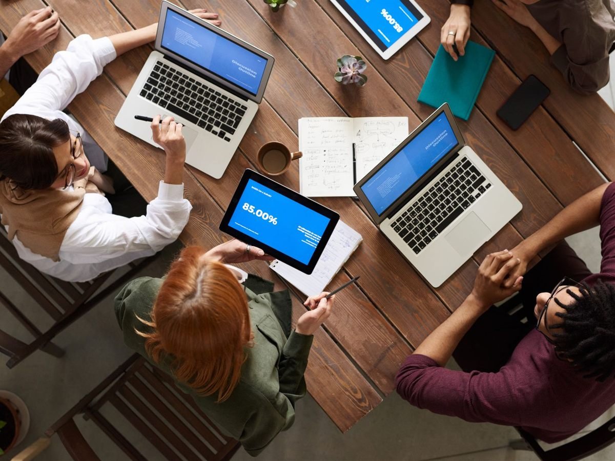Equipe em volta de uma mesa, vista de cima, com indicadores nas telas dos notebooks